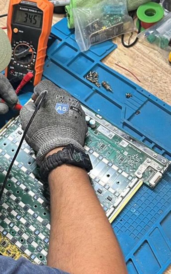 Gloved technician probing an ASIC control board with a multimeter